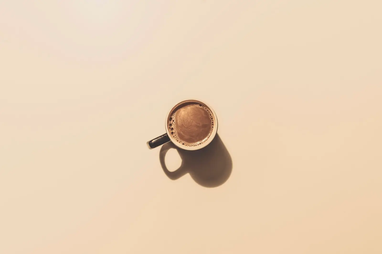 A small cup of coffee on a pale peach background