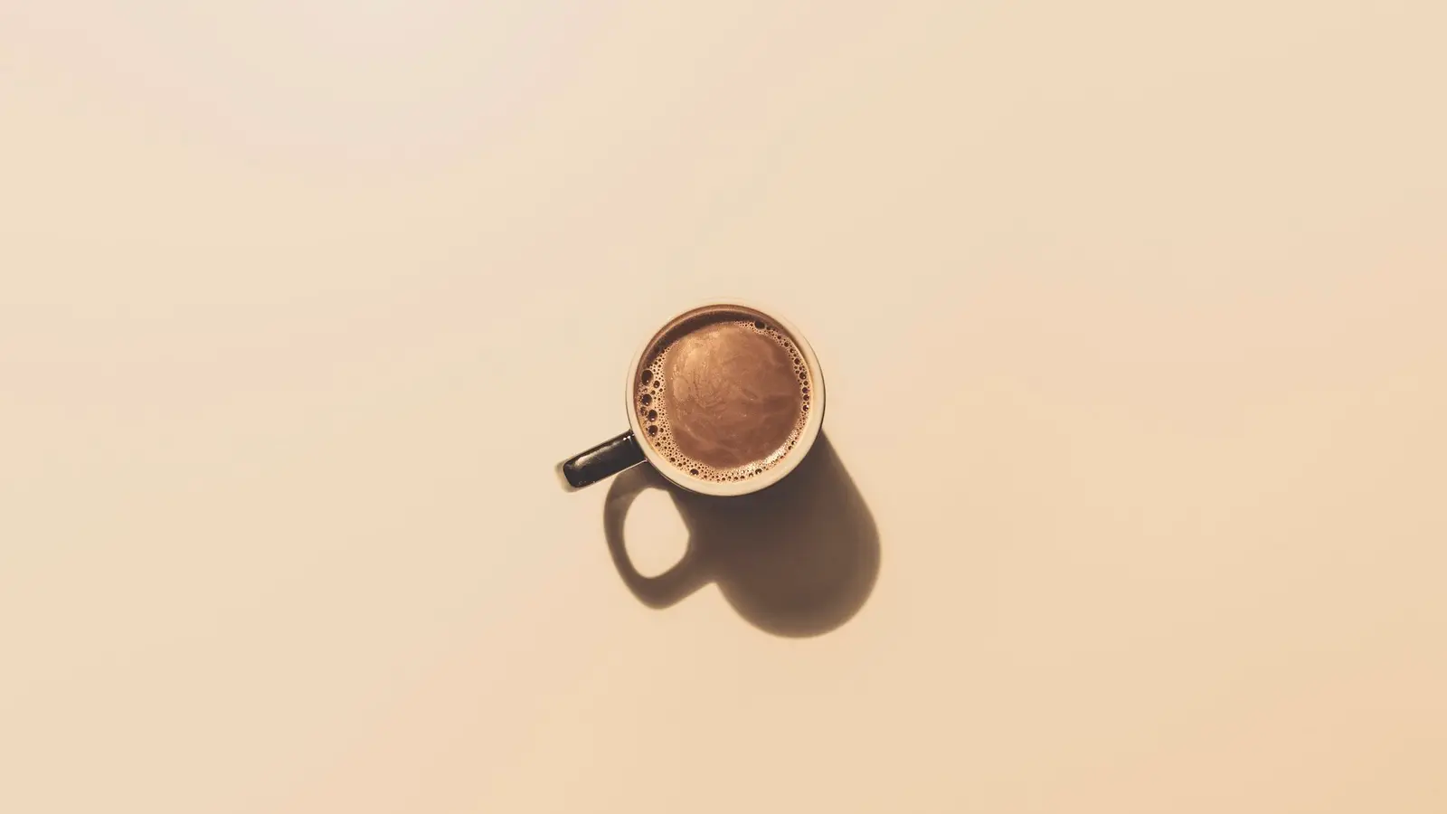 A small cup of coffee on a pale peach background