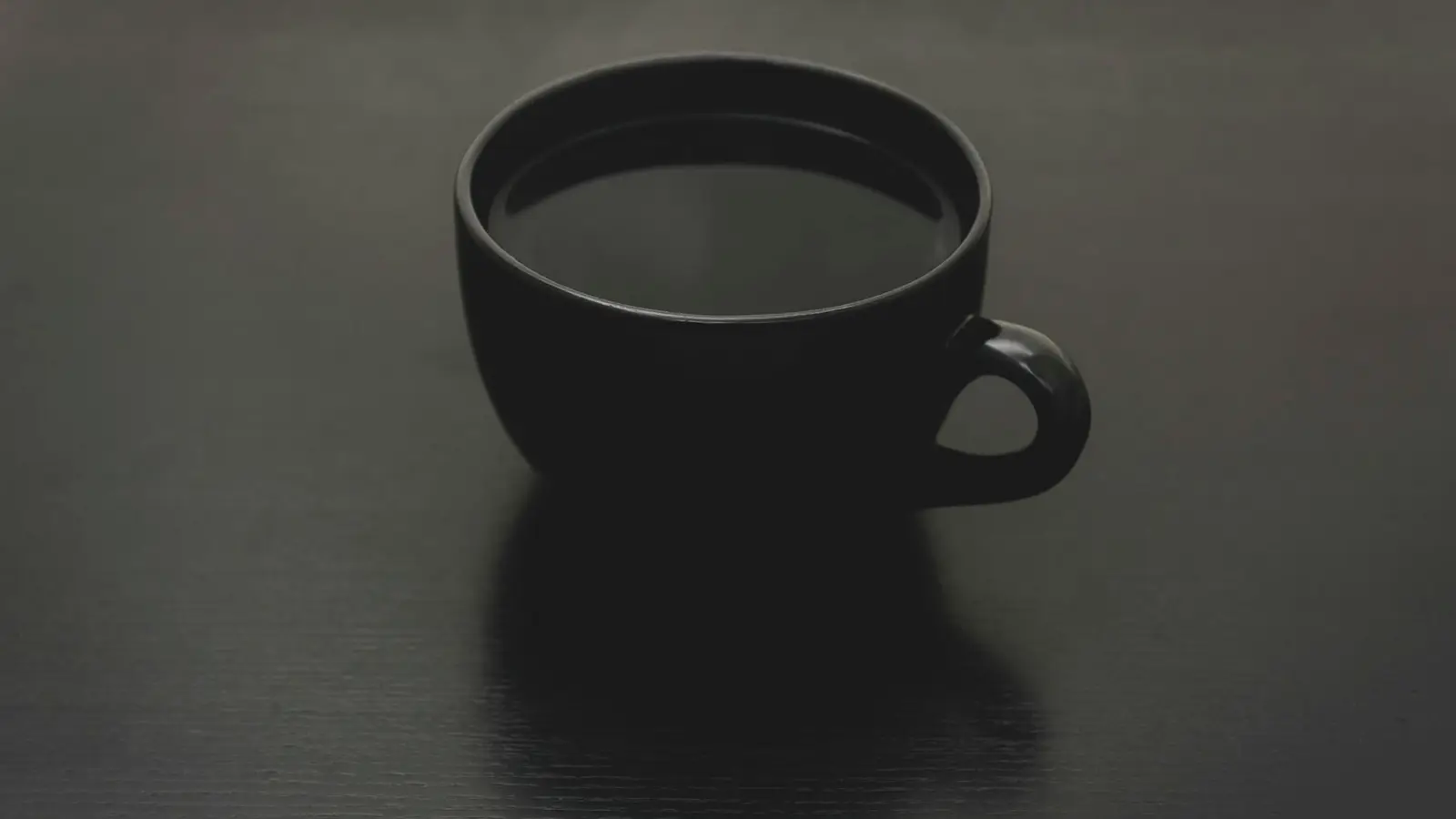 A dark cup of black coffee on a dark surface