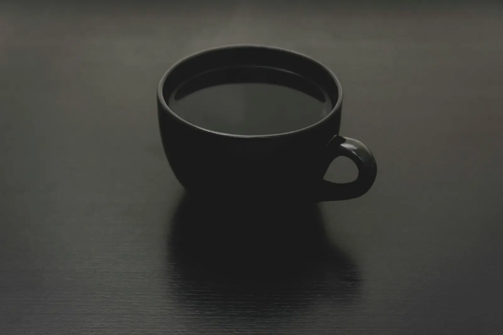 A dark cup of black coffee on a dark surface