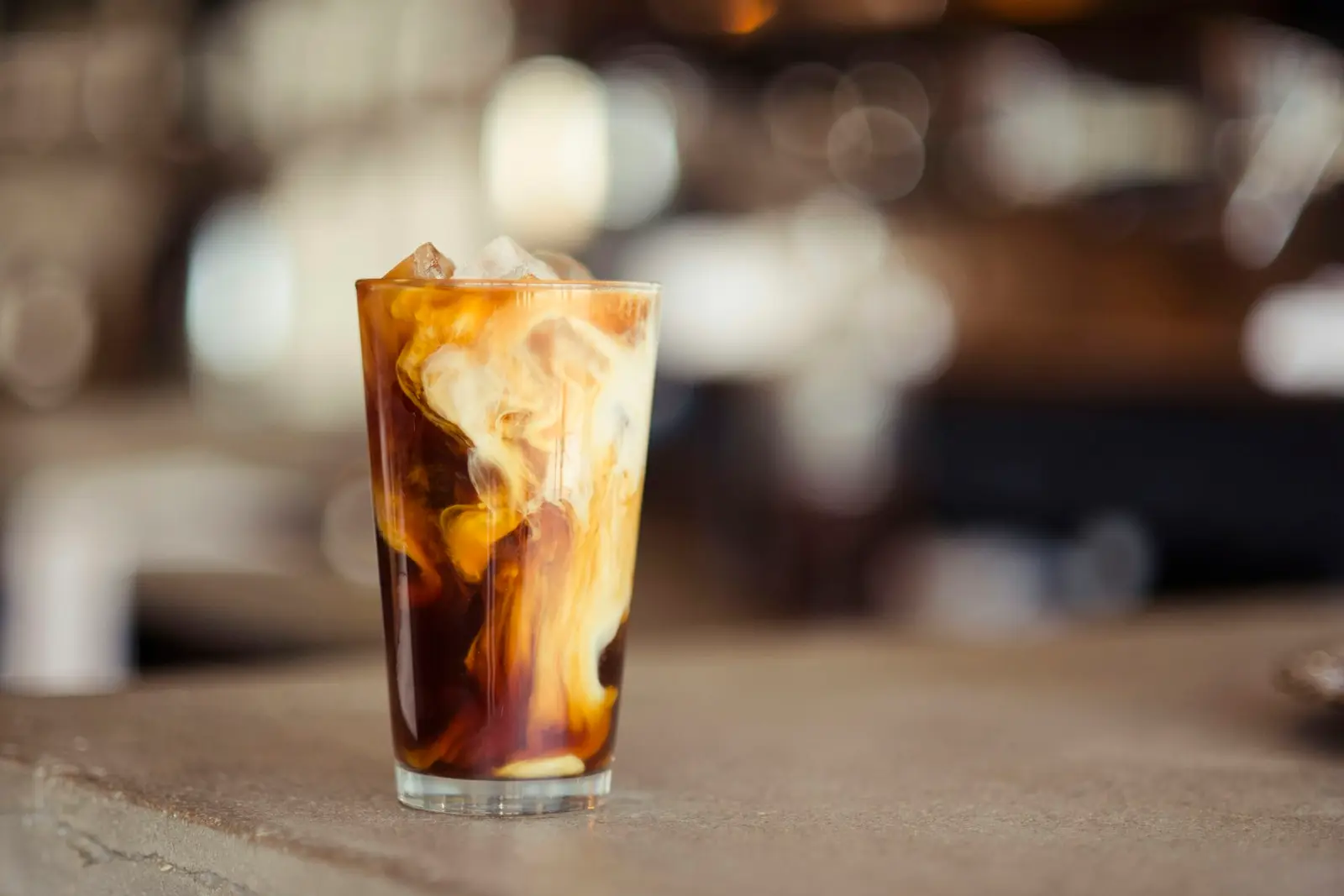A tall glass of iced coffee with milk on a wooden table