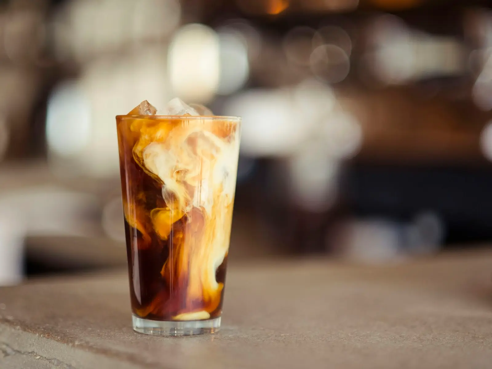 A tall glass of iced coffee with milk on a wooden table