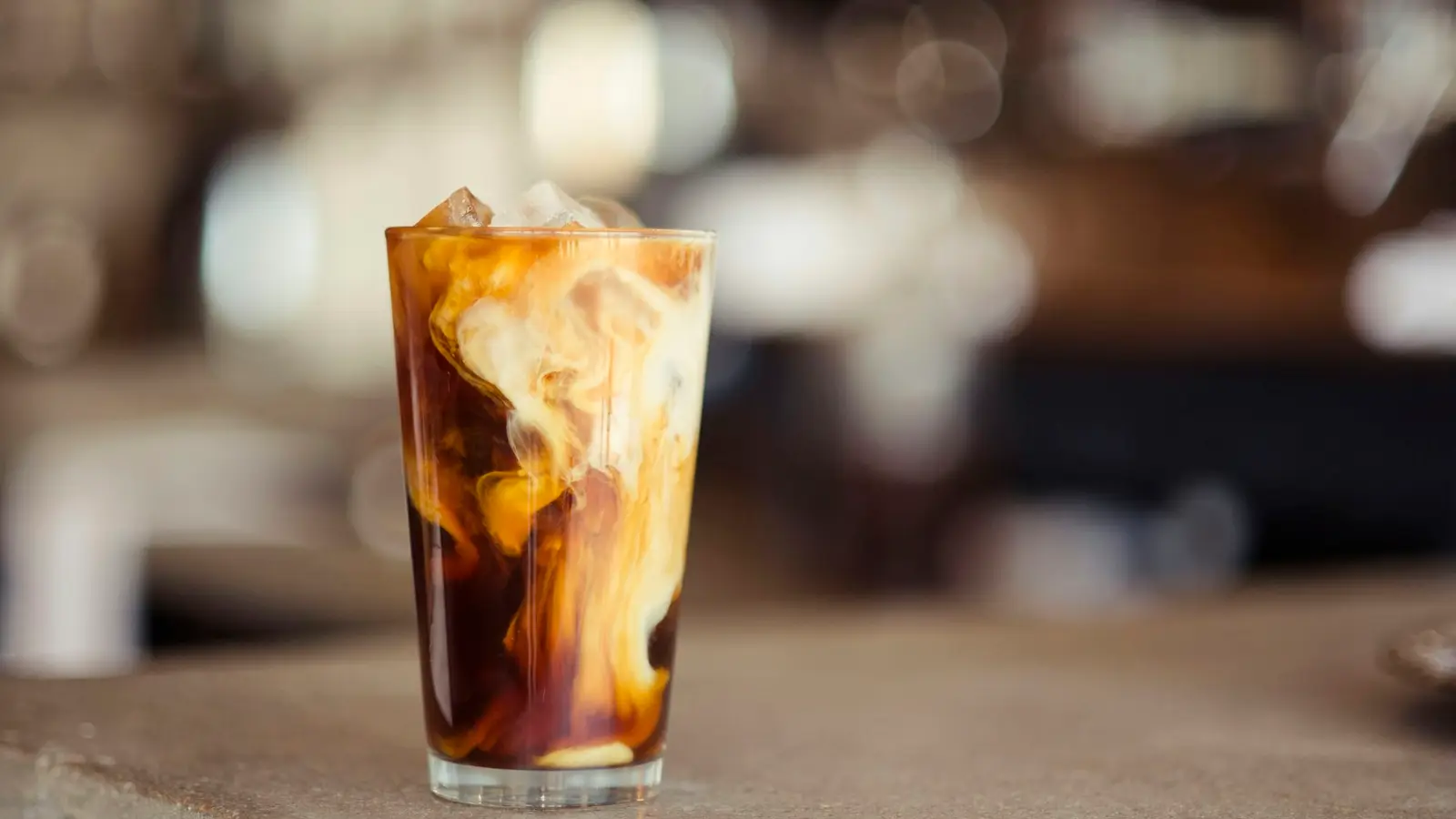 A tall glass of iced coffee with milk on a wooden table