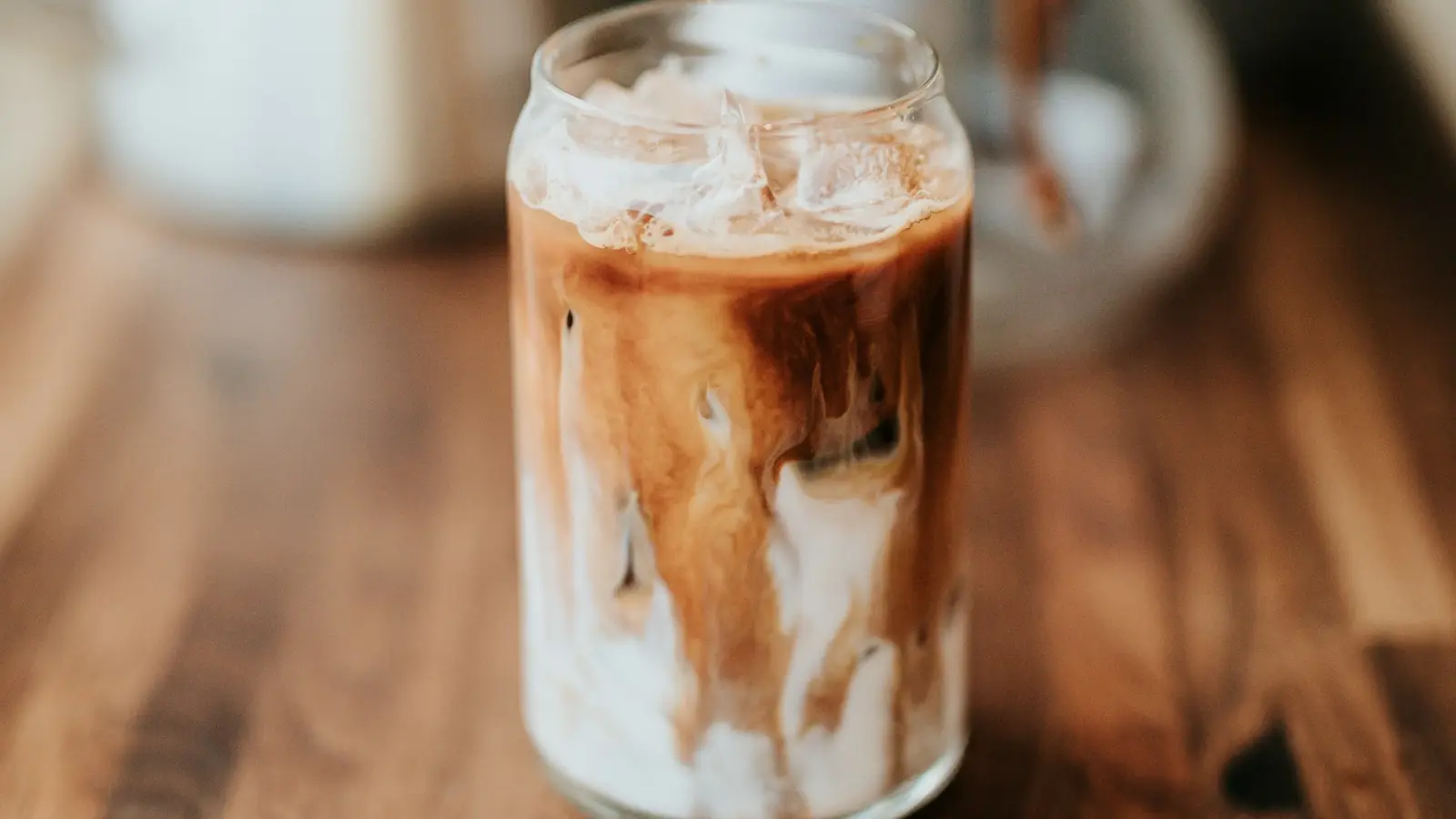 An iced milk coffee in a glass jar on a wooden counter