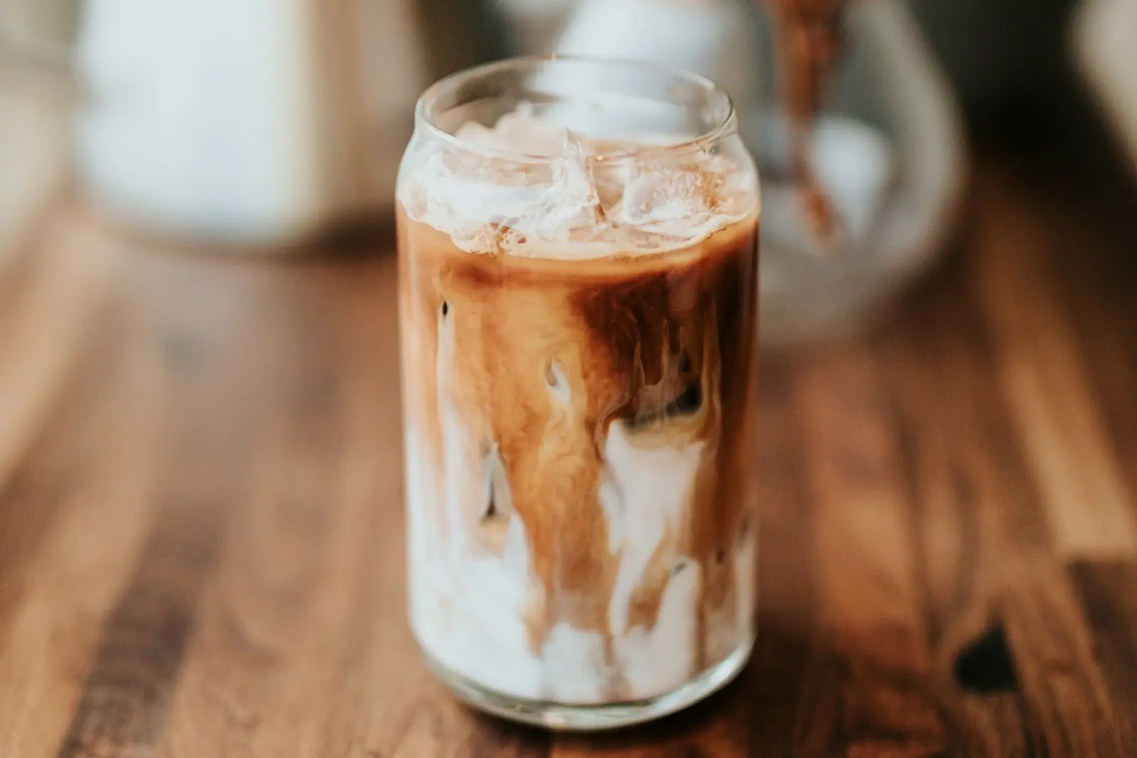 An iced milk coffee in a glass jar on a wooden counter