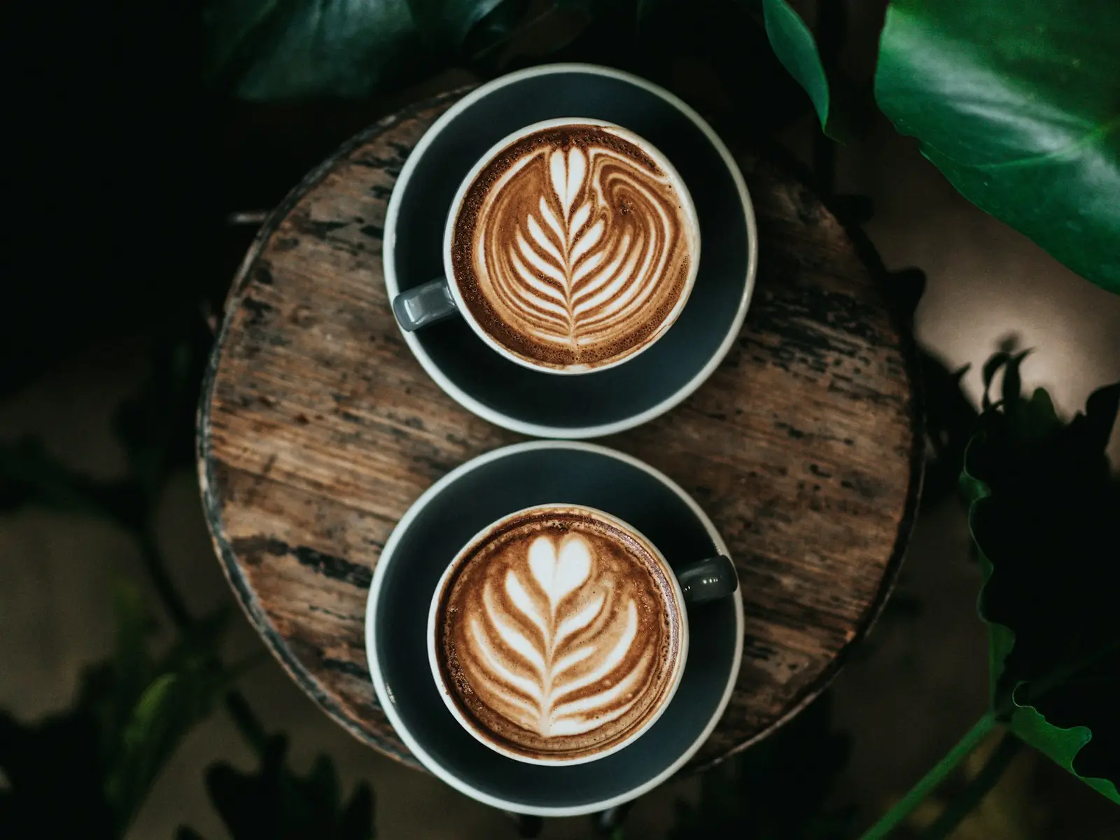 Two cups of latte with leaf art on a wooden tray