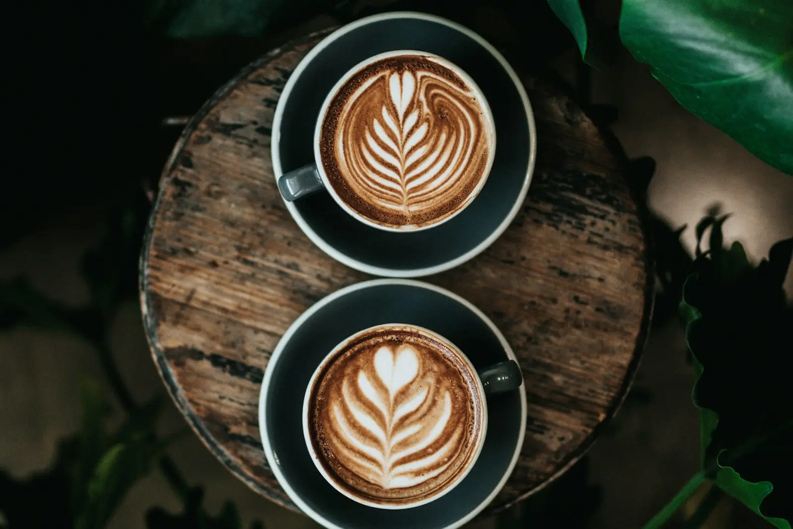 Two cups of latte with leaf art on a wooden tray