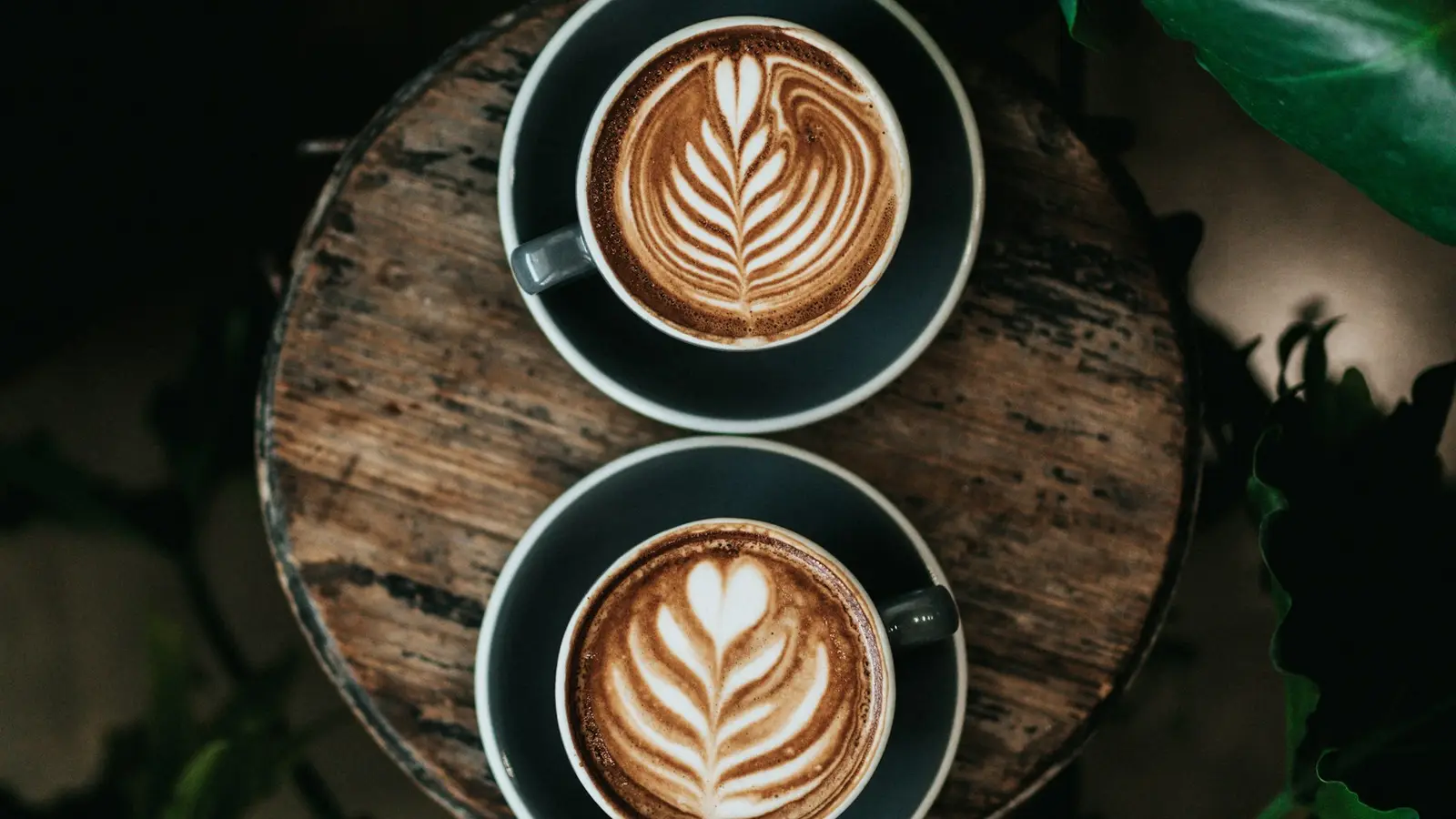 Two cups of latte with leaf art on a wooden tray