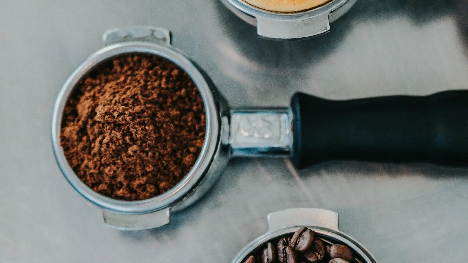 A portafilter filled with ground coffee beside beans