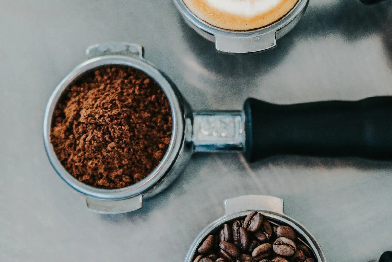 A portafilter filled with ground coffee beside beans
